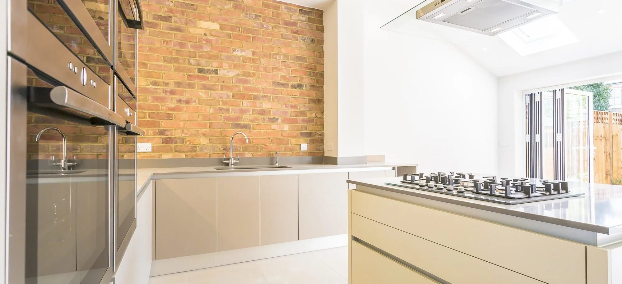 Sleek minimalist kitchen with cream cabinets and brick feature wall